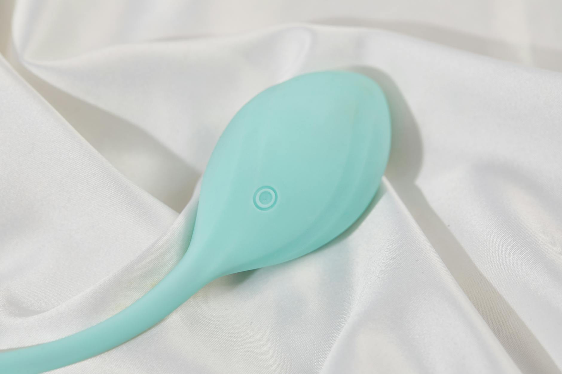 A sleek teal silicone vibrator resting on white silk fabric, symbolizing luxury self-care