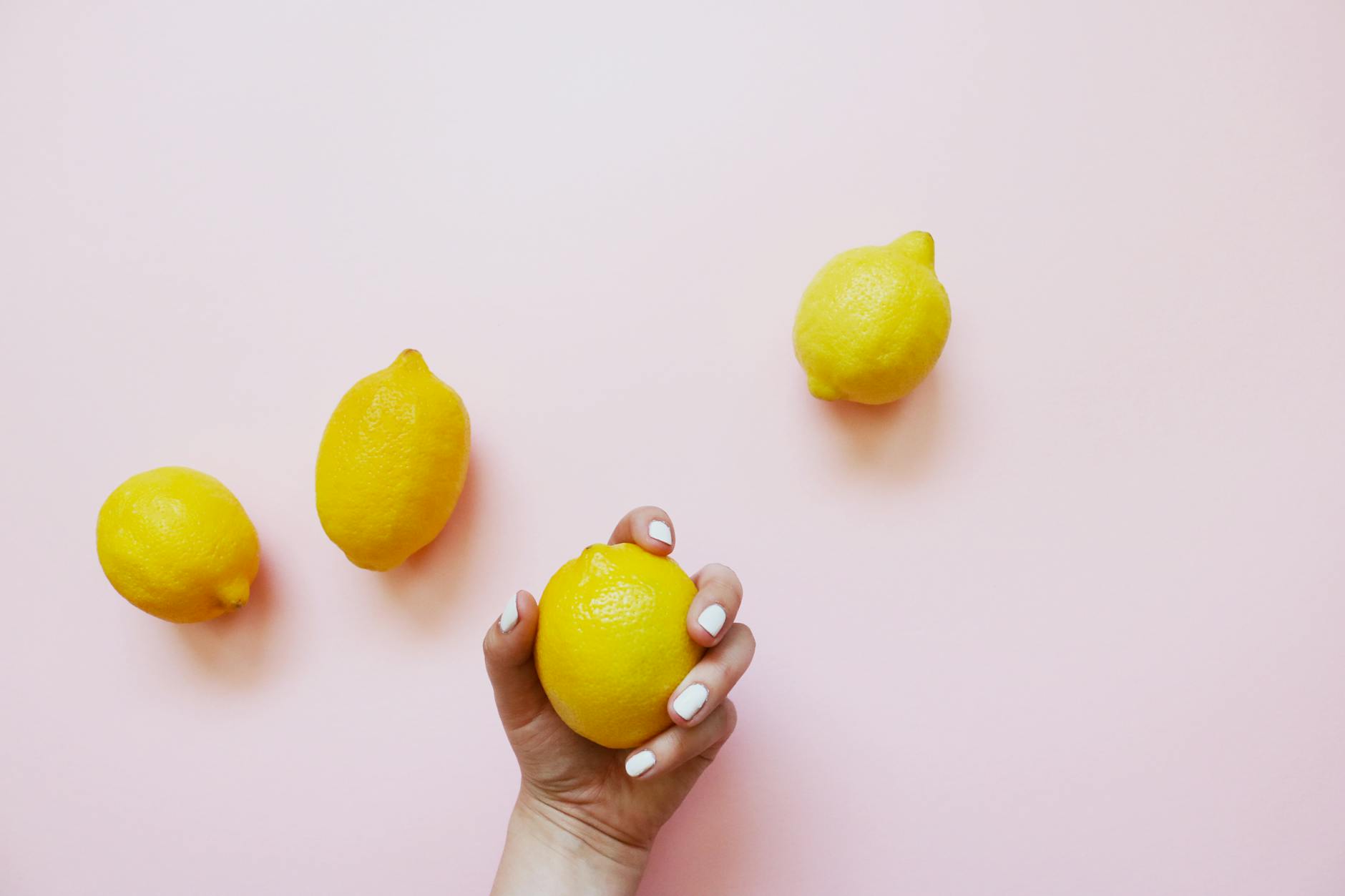 A hand holding a lemon on a soft pink background, symbolizing slow, intentional arousal building.