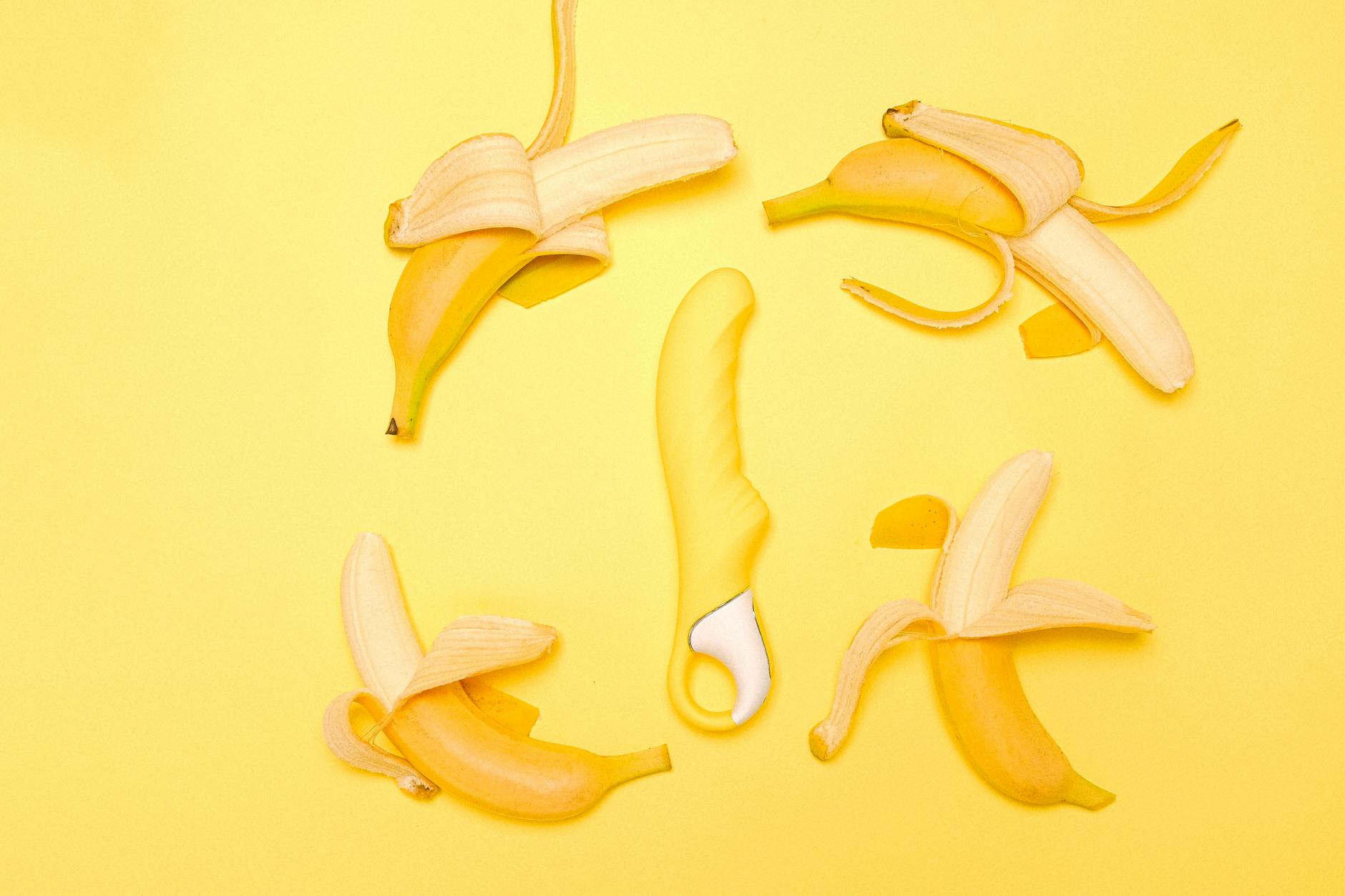 Yellow lemon clitoral vibrator surrounded by fresh lemons on a bright yellow surface