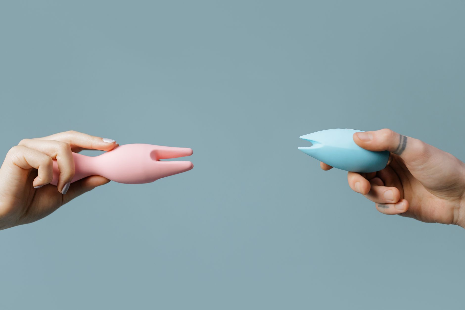 Two hands holding colorful silicone clitoral vibrators side by side