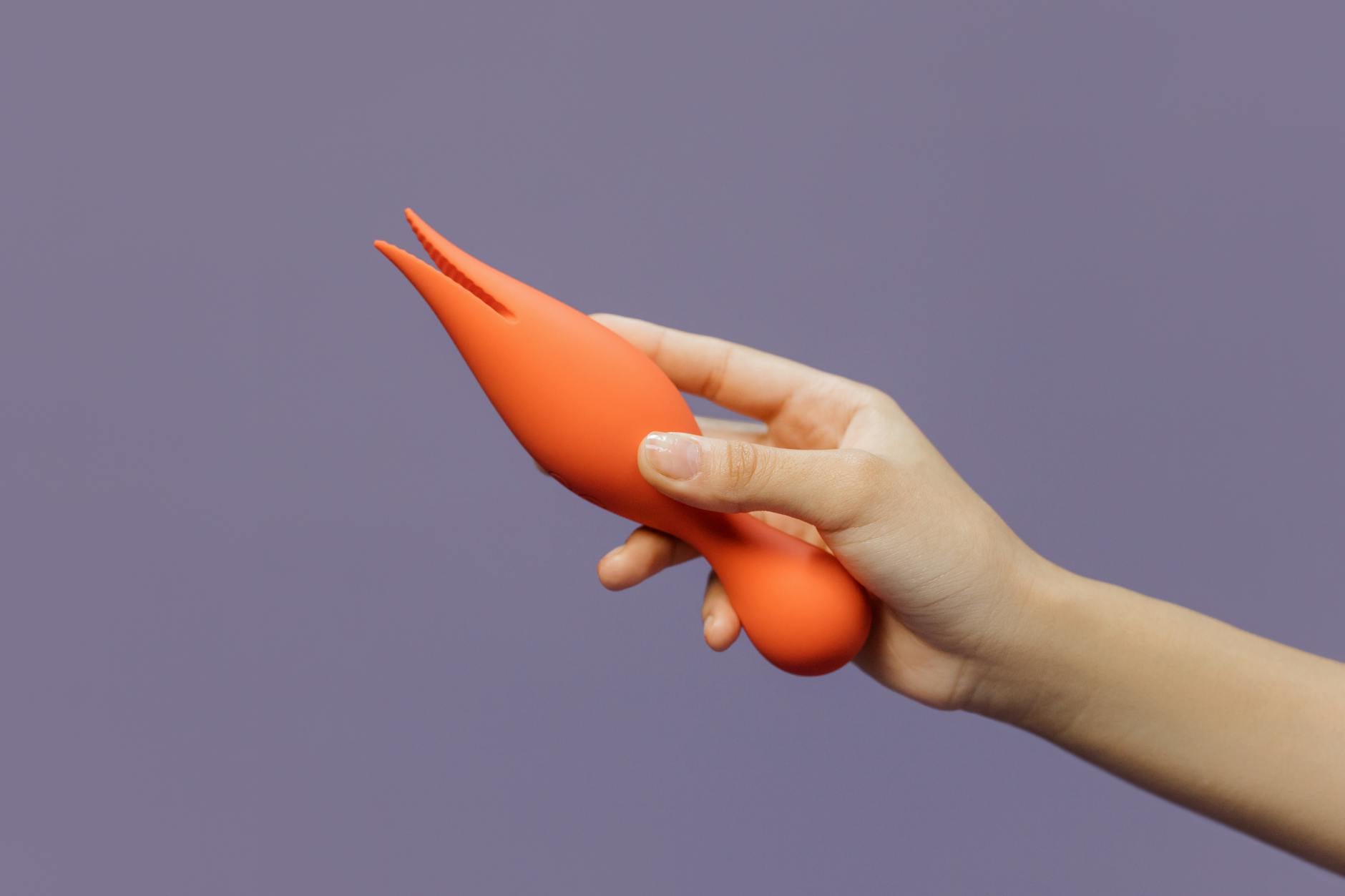 Hand holding a lemon-colored clitoral vibrator against a minimalist purple background