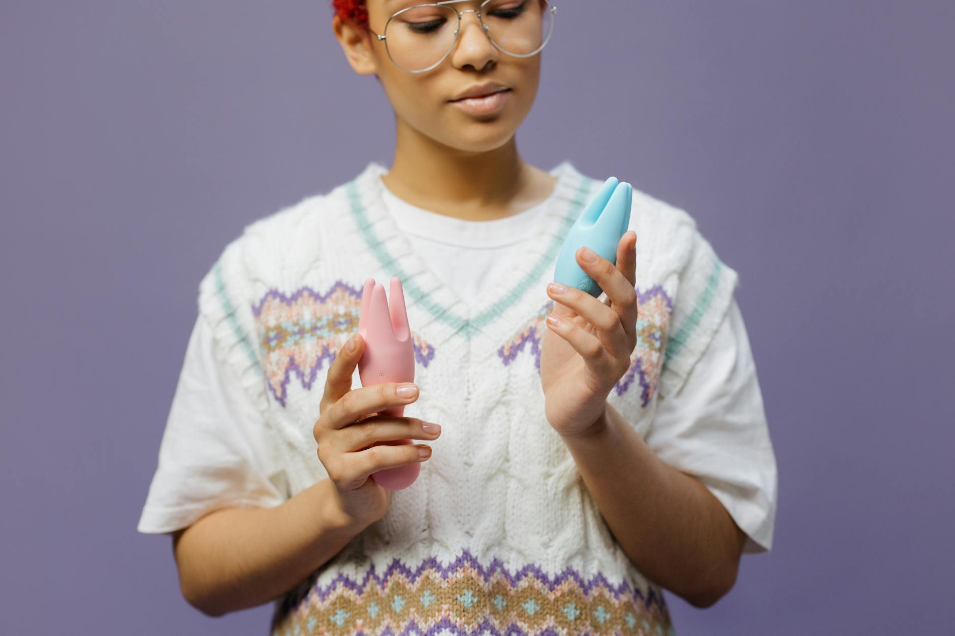 Woman holding blue and pink silicone vibrators with a thoughtful expression, exploring options for the first time