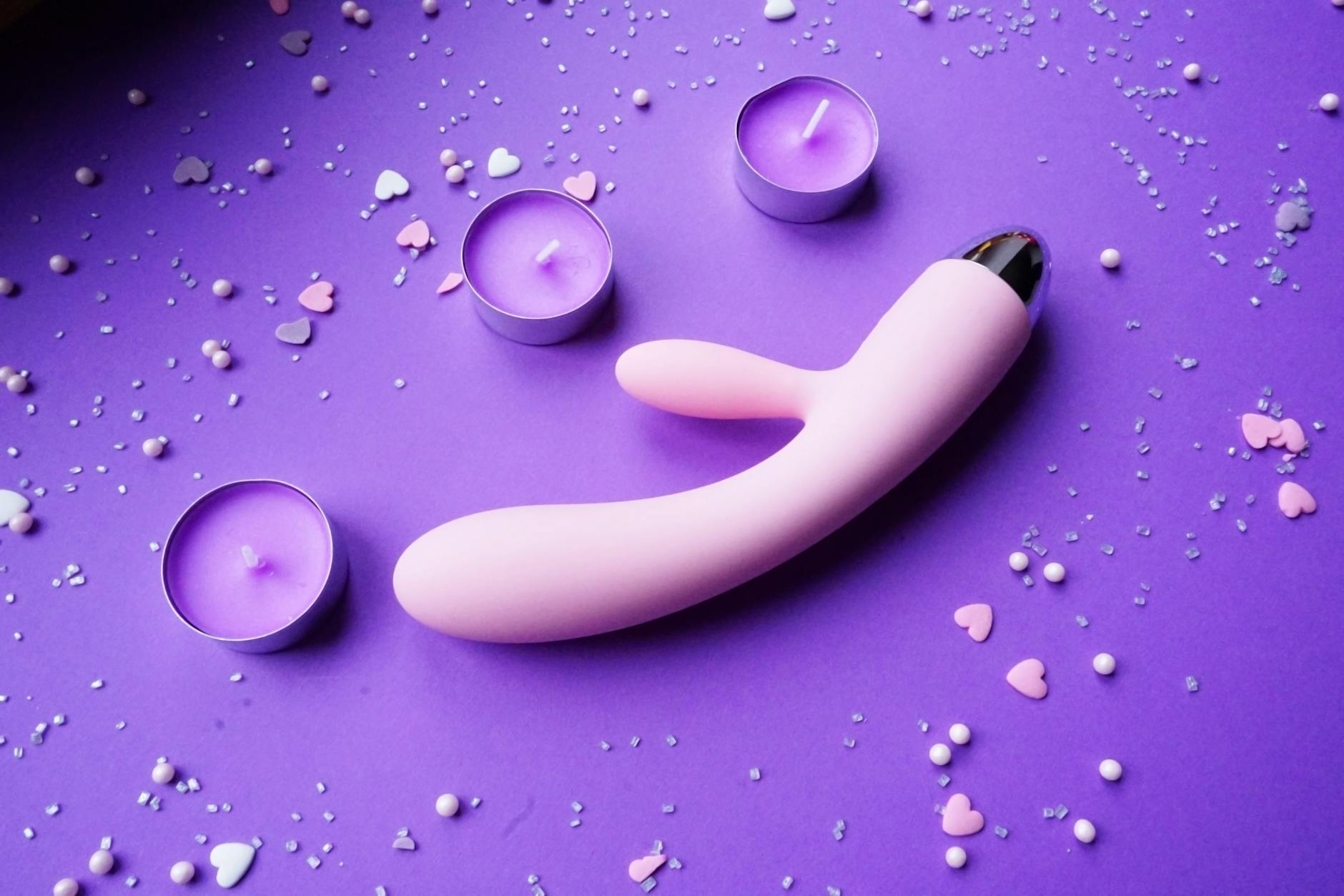 Pink vibrator arranged with heart confetti and candles on a romantic surface